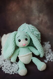 cute light green rabbit with big ears handmade in white diaper in studio with knitting threads on background