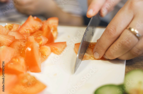 A little boy cuts a tomato with a knife.