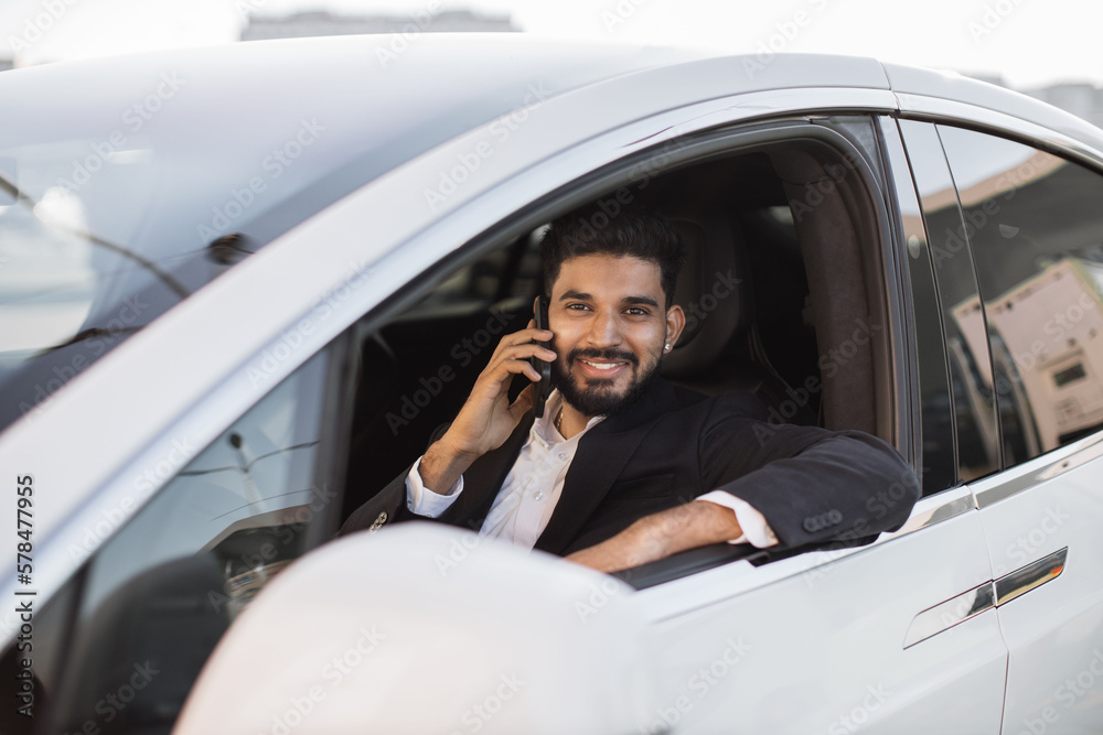 Attractive bearded man in formal suit talking on smartphone while sitting inside brand new auto. Well-dressed indian man smiling happily while looking out of open car window outdoors. Attractive bearded man in formal suit talking on smartphone while sitting inside brand new auto. Well-dressed indian man smiling happily while looking out of open car window outdoors.