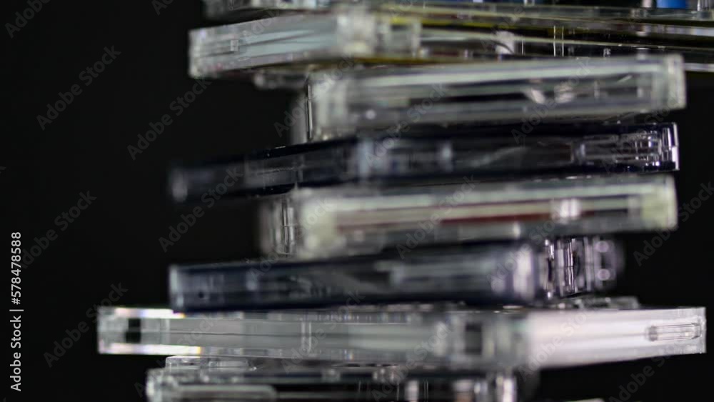 A stack of audio cassettes spins on a black background and mirror surface. Golden nineties. A stack of audio cassettes spins on a black background and mirror surface. Golden nineties.