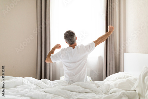 Rear view of mature man in pajamas stretching in bed