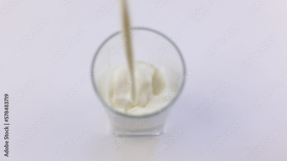 white fresh milk is poured into a transparent glass on a white background