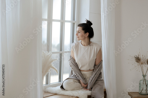 Dunkelhaarige Frau sitzt entspannt am Fenster