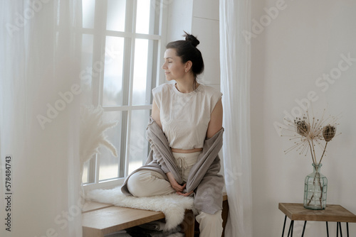 Dunkelhaarige Frau sitzt entspannt am Fenster