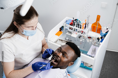 Consultation with dentist at dentistry. Teeth treatment. Dentist examines african man mouth and teeth and treats toothaches. African man patient of dentistry.