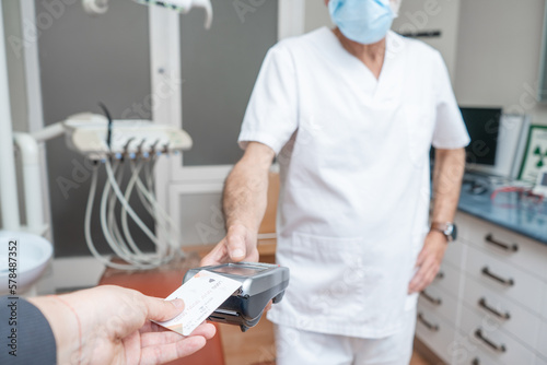 Adult woman paying for visit in dentist office in the medical clinic with card
