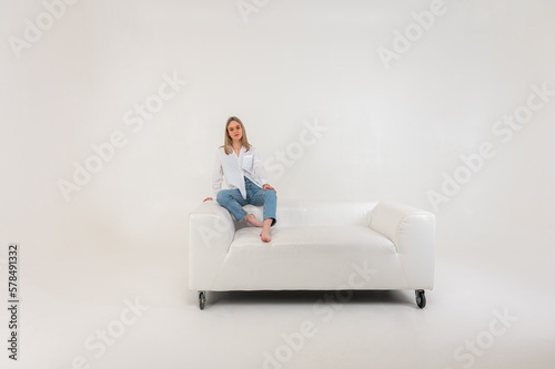 Happy young girl relaxes on comfortable soft white leather sofa, calm contented girl stretches on sofa, thinking about pleasant things. Isolated on light background, place for inscription