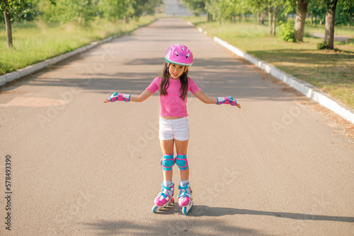 A disappointed girl in a protective sports helmet and roller skates throws up her hands. The child unsuccessfully learns to rollerblade photo