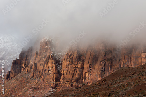 Low winter storm clouds cover the tops of the Red Mountains north of Ivins Utah, USA causing shadows and light to play across the surface of the deep red sandstone cliffs on a chilly stormy winter day