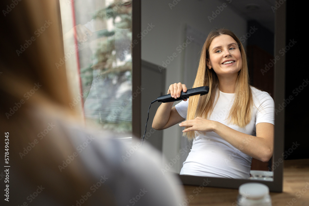 Smiling confident pregnant woman straightening hair using electric