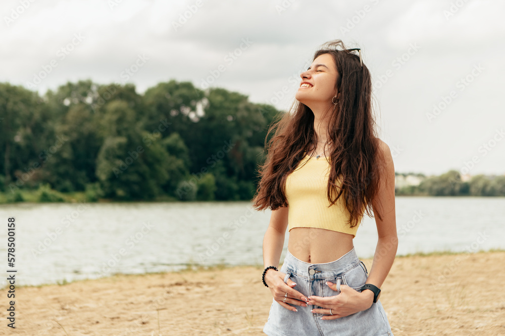 Fototapeta premium Slim woman stand on the blanket coverlet near river sea lake. Female on beach island with splashing waves and foam. Girl tourist vacation, weekend relaxing resting resort. Lady go on shore, sunbathing