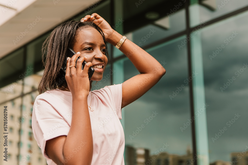 Fototapeta premium African american woman hold hand phone surfing internet chatting friends colleague call order taxi or food standing talking phone speaking outside street smiling happy positive good mood 