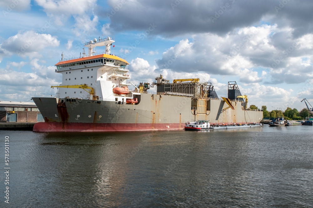 A tugboat is tethered to a heavy industrial ship docked in the Netherlands.