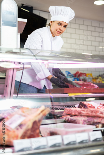 Young female butcher cutting big piece of beef meat in butchery