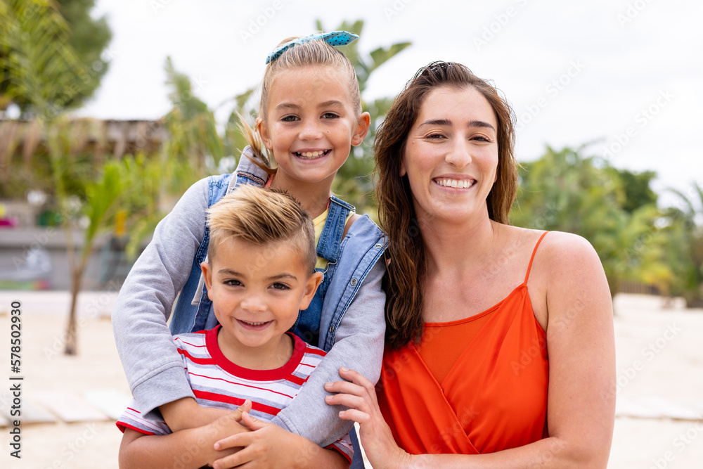 Portrait of happy biracial mother and children embracing and smiling at beach - obrazy, fototapety, plakaty 