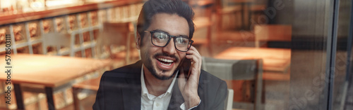 Smiling indian businessman is talking phone with client during lunch time in cozy cafe