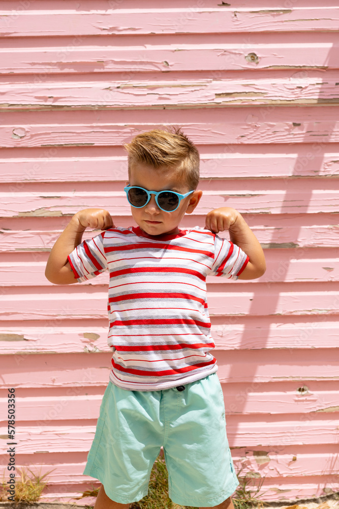 Portrait of happy biracial boy smiling and showing muscles over pink wall - obrazy, fototapety, plakaty 