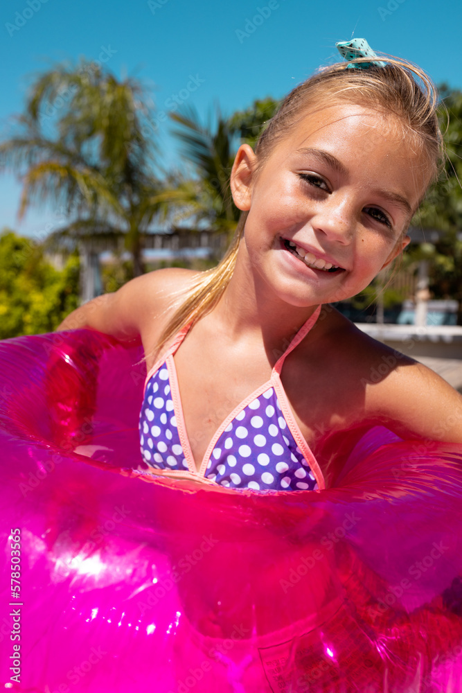 Portrait of happy biracial girl smiling and holding swim ring by the swimming pool - obrazy, fototapety, plakaty 