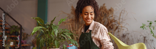 Smiling woman florist taking care of plant watering it in floral shop