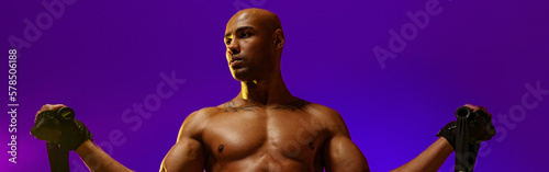 Sporty man performs exercises with expander on violet studio background. Strength and motivation © Kostiantyn