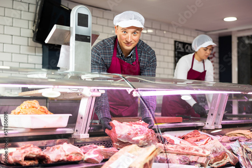 Adult male seller in uniform puts beef ribs in showcase
