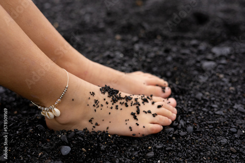 Two kid feet in the beach with black sand because of a volcano in Tenerife, Canary islands.