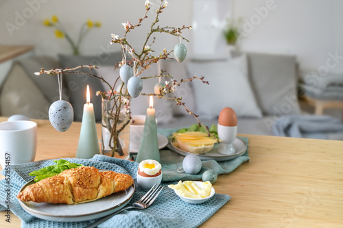 Breakfast table with boiled egg, croissant and pastel turquoise Easter decoration in a small living room, copy space, selected focus