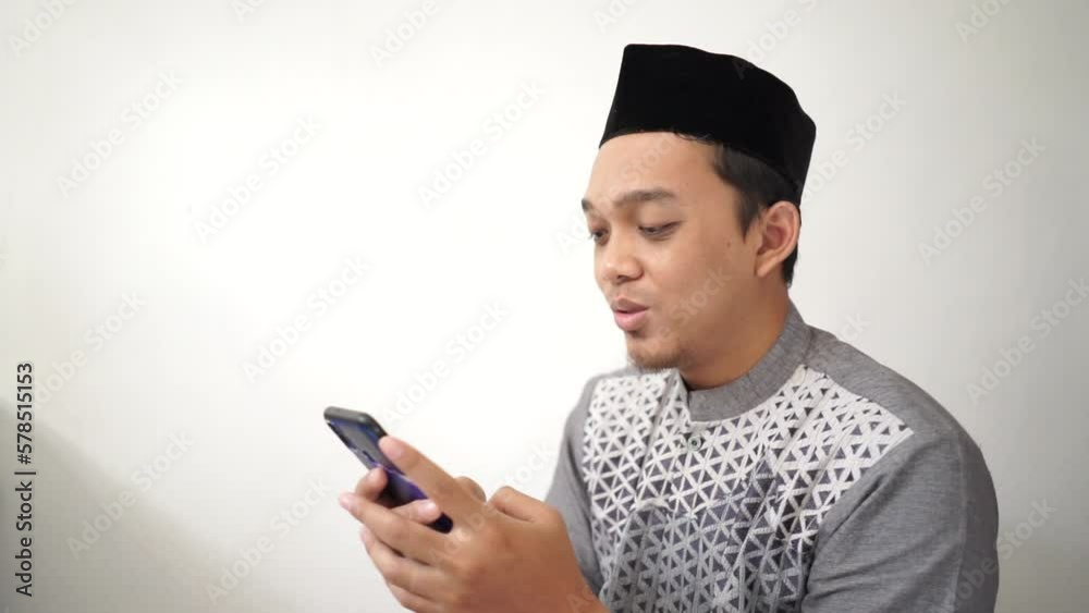 Indonesian Asian muslim man smiling and looking at smartphone wears black hat called peci or songkok