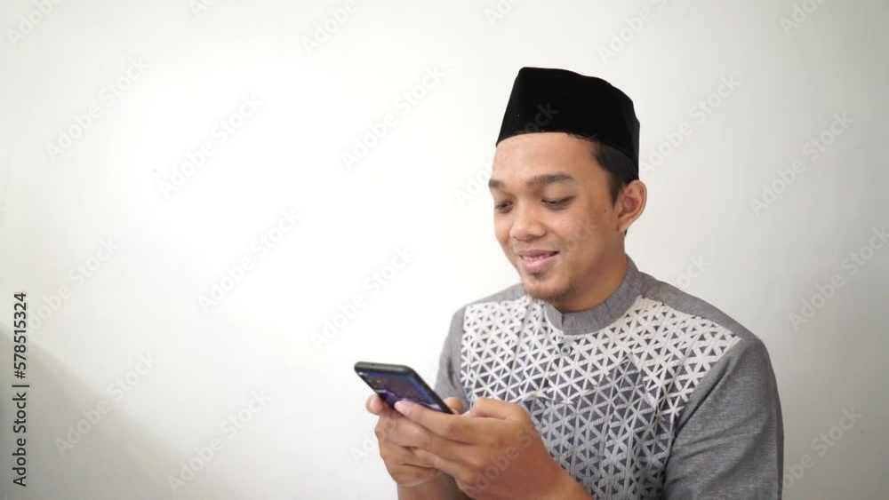 Indonesian Asian muslim man smiling and looking at smartphone wears black hat called peci or songkok
