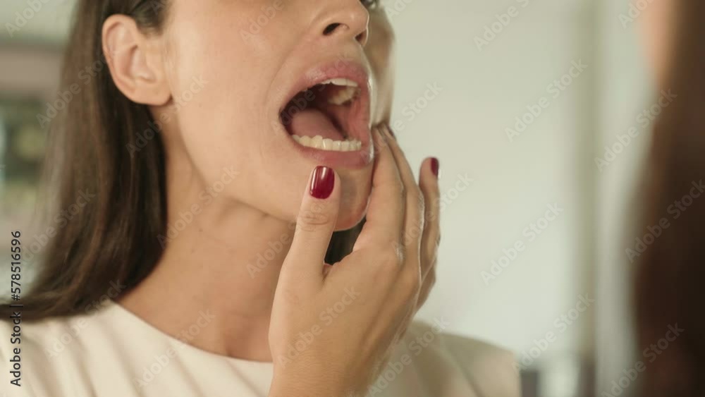 Woman checking her teeth in mirror with opened mouth looking for caries in bathroom at home. Teeth health care concept.
Woman checking her teeth in mirror with opened mouth looking for caries in bathroom at home. Teeth health care concept.