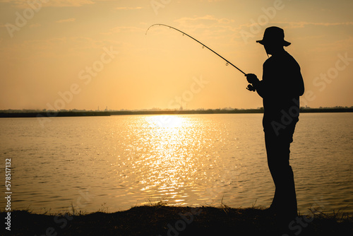 Silhouette of young man fishing on a lake during at sunrise.