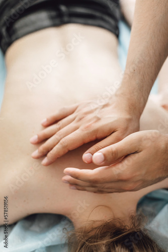Male masseur with strong hands professionally massaging scapulas and shoulders. Beautiful naked young woman with perfect skin getting back massage at spa salon.
