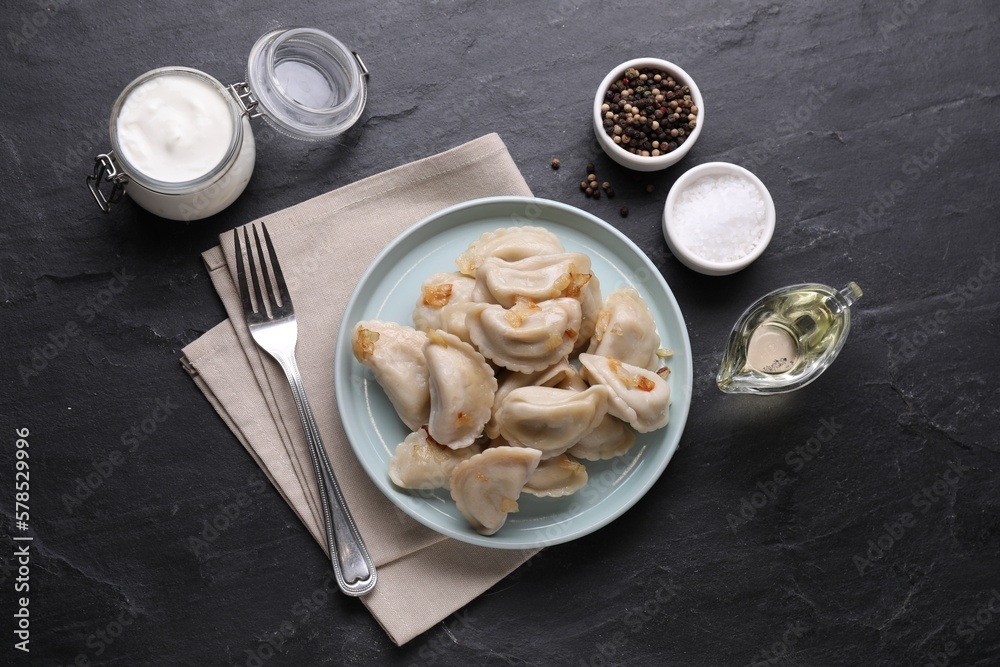 Delicious dumplings (varenyky) with potatoes and onion served on black table, flat lay