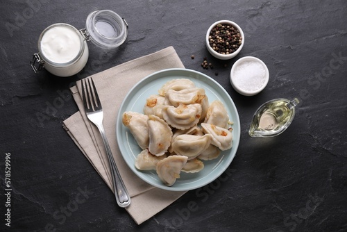 Delicious dumplings (varenyky) with potatoes and onion served on black table, flat lay