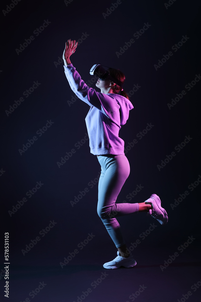 Pretty young woman in VR glasses throwing virtual ball on black background