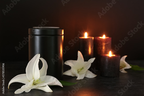 Mortuary urn, white lily flowers and burning candles on dark background