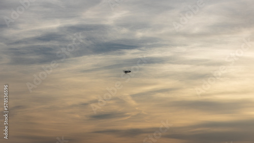 small biplane flies against clouds at sunset