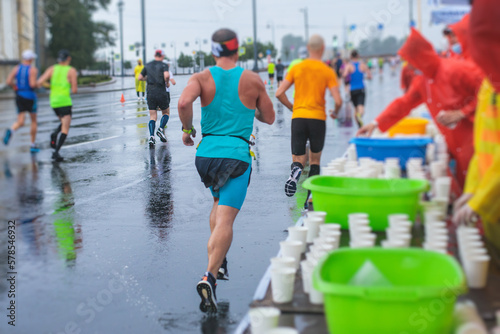 Marathon runners crowd, participants start running the half-marathon in the city streets, crowd of joggers in motion, group athletes outdoor training competition in the rain