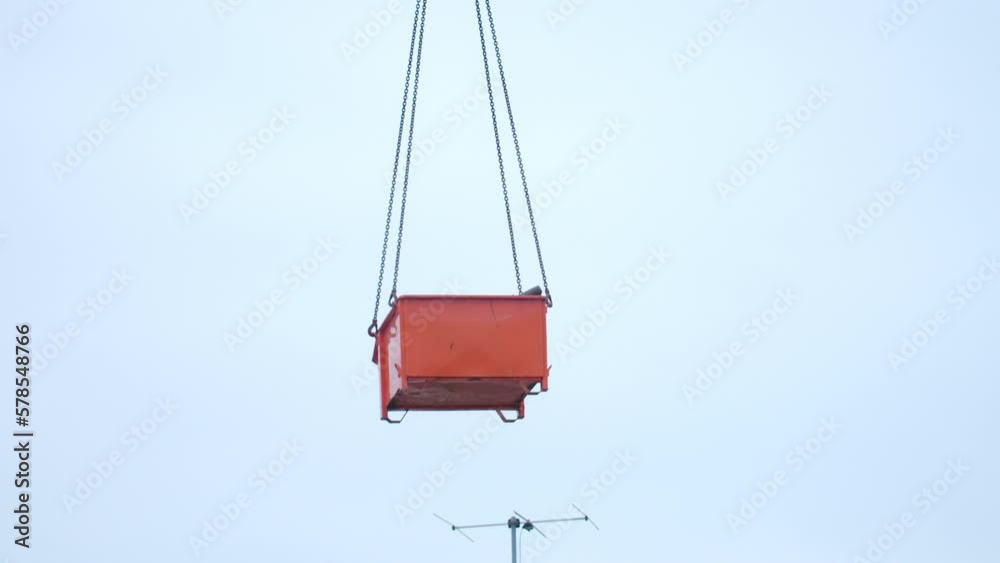 Medium wide shot of a green container filled with roof tiles and debris getting lifted by a crane. Medium wide shot of a green container filled with roof tiles and debris getting lifted by a crane.