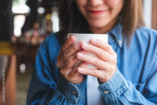 Closeup image of a young woman holding and drinking hot coffee in cafe
