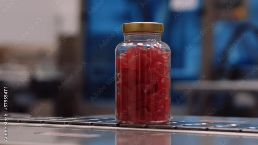 Red multivitamin supplement gummies in clear bottles on conveyor belt