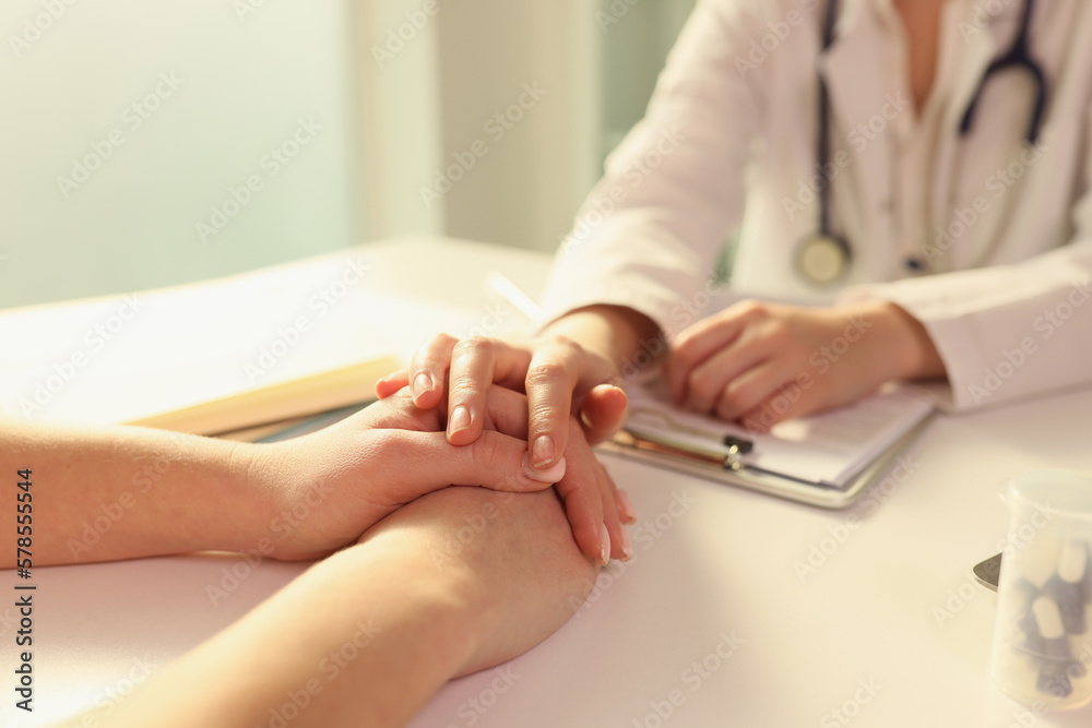 Doctor puts her hand on hands of patient, sitting with her in medical clinic.