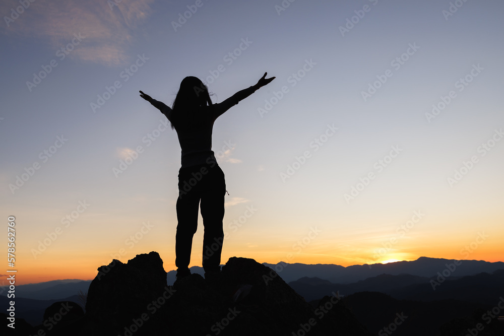 © Tinnakorn - Silhouette of woman on top of the mountain looking to the sun, freedom, pray on top of mountain.