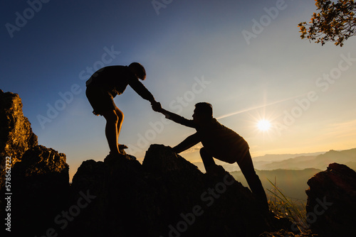  Silhouettes of two people climbing on mountain and helping. Help and assistance concept.