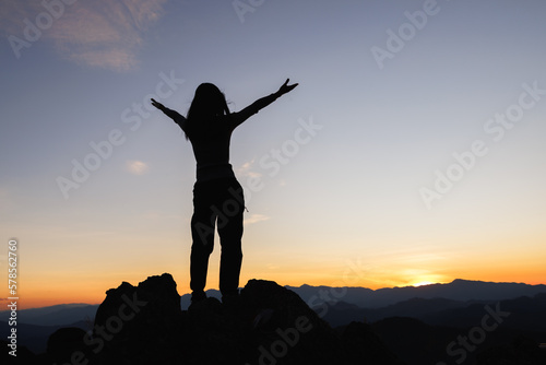 Silhouette of woman on top of the mountain looking to the sun  freedom  pray on top of mountain.