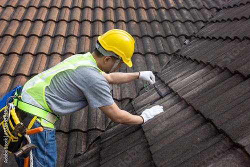 Worker man using waterproof roof coating repair to fix crack of the old tile roof. photo