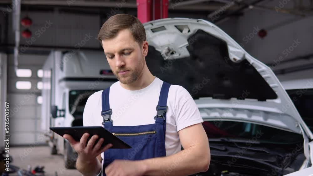 Professional car mechanic working in auto repair service with tablet. Computer diagnostics of the electric car in garage. Car maintenance service concept