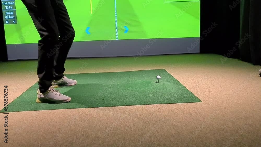 Golf player playing golf indoors on golf simulator closeup. Driving range with screen for golf and golfer legs