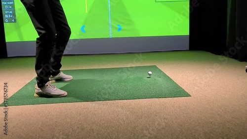 Golf player playing golf indoors on golf simulator closeup. Driving range with screen for golf and golfer legs photo