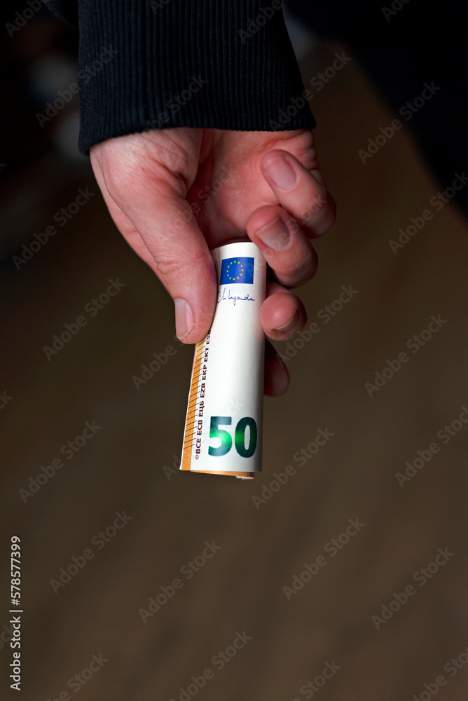 Rolled euro money in hand on a dark background.
